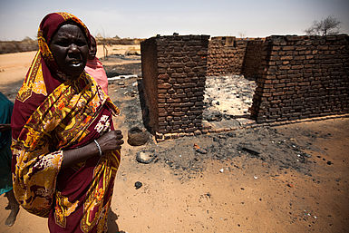 Eine Frau steht vor ihrem zerstörten Haus in Darfur