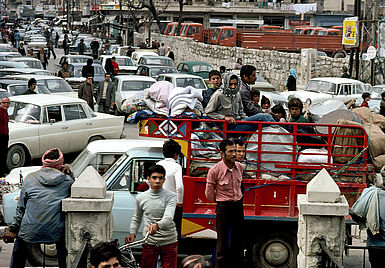 Eine Straße voller Autos und Menschen, Flüchtlinge sitzen mit ihren Habseligkeiten teilweise auf den Autos.