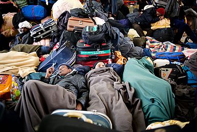 Flüchtlinge schlafen eng zusammenliegend neben ihren Koffern und Habseligkeiten.